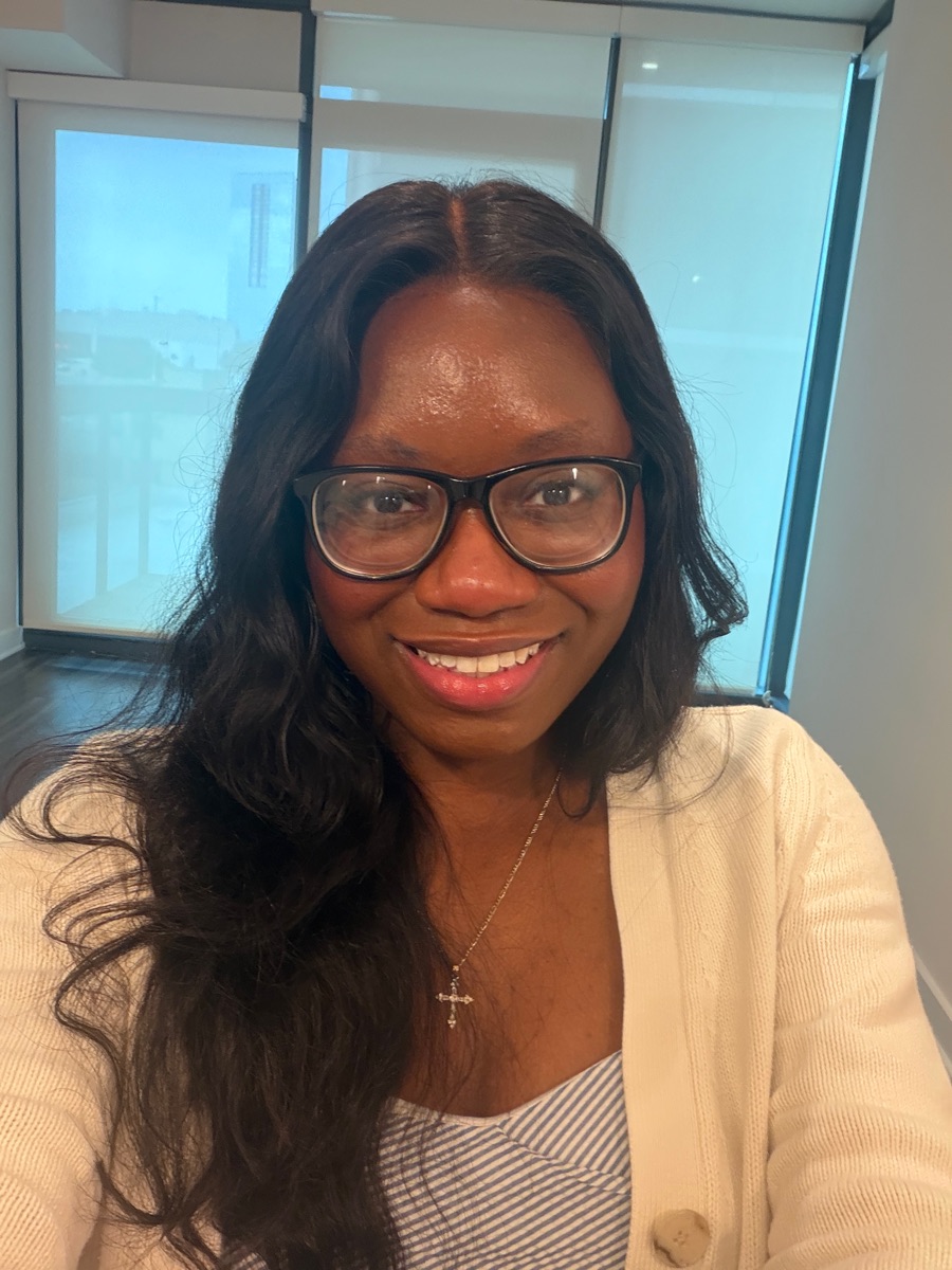 Tomi today, smiling in glasses and a cream cardigan